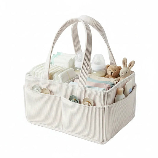 Beige corduroy baby diaper caddy with handles, filled with diapers, bottles, clothes, pacifiers, and toys.