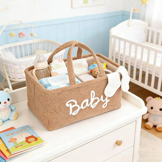 Brown fleece baby diaper caddy with "Baby" text, handles, and compartments, filled with essentials on a changing table.