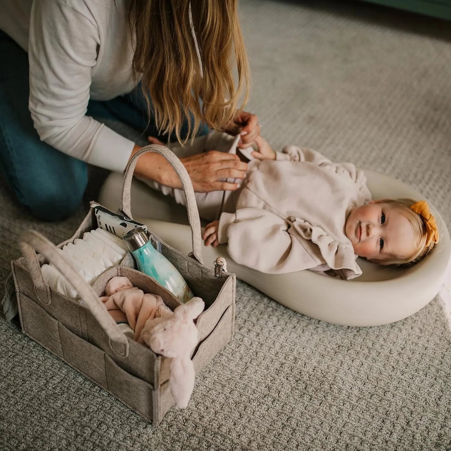 Gray felt portable diaper caddy with compartments, next to a baby on a changing pad.