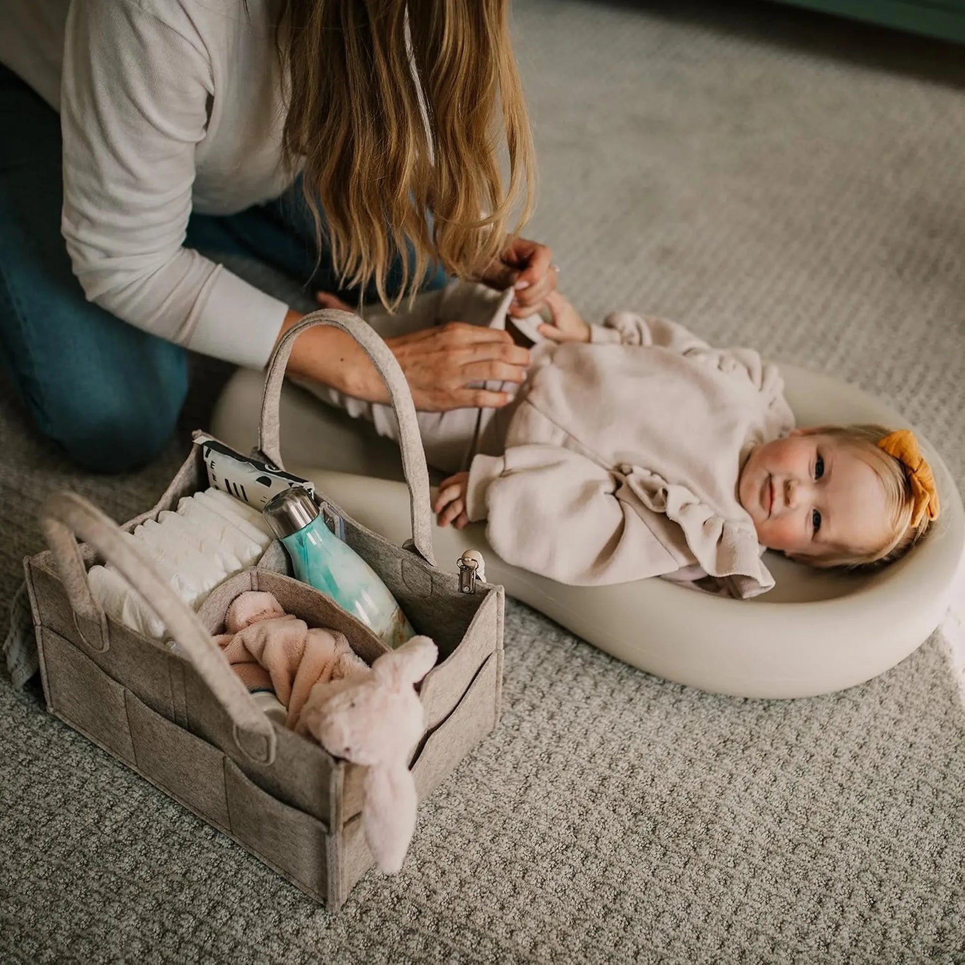 Gray felt portable diaper caddy with compartments, next to a baby on a changing pad.