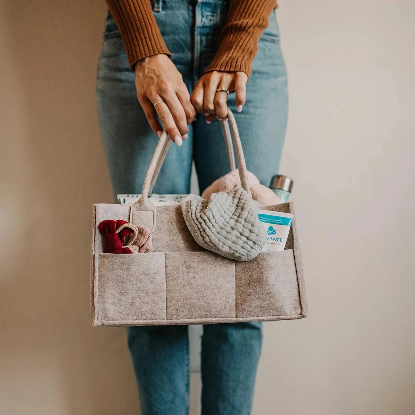 Beige felt diaper caddy with handles, holding baby essentials, carried by a person in jeans.
