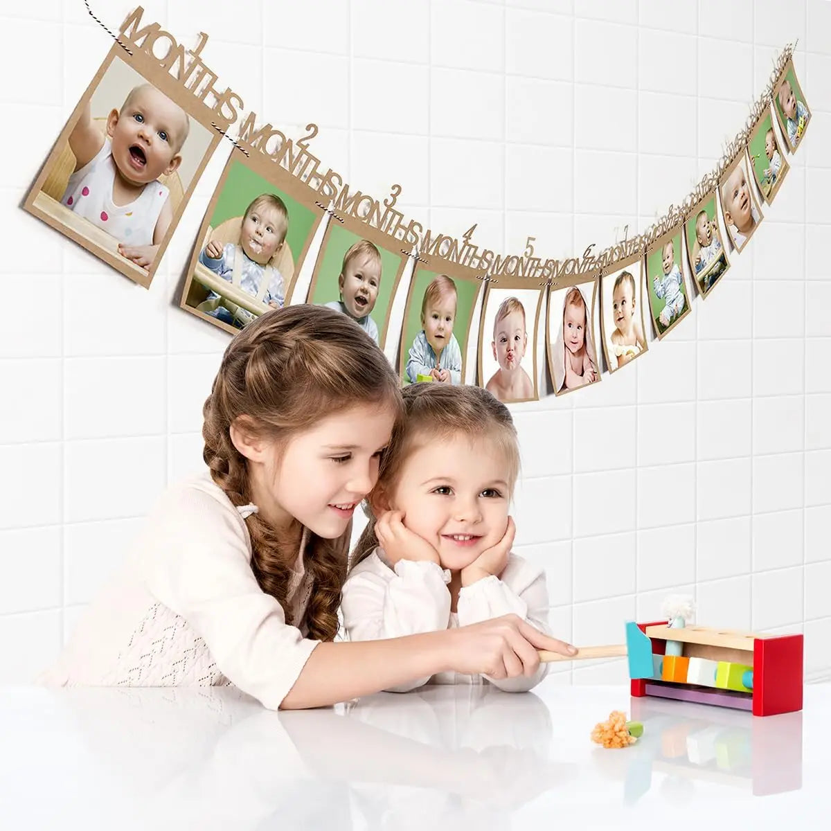 Kraft paper baby's first year photo banner with 12 monthly frames, displayed above two smiling girls.