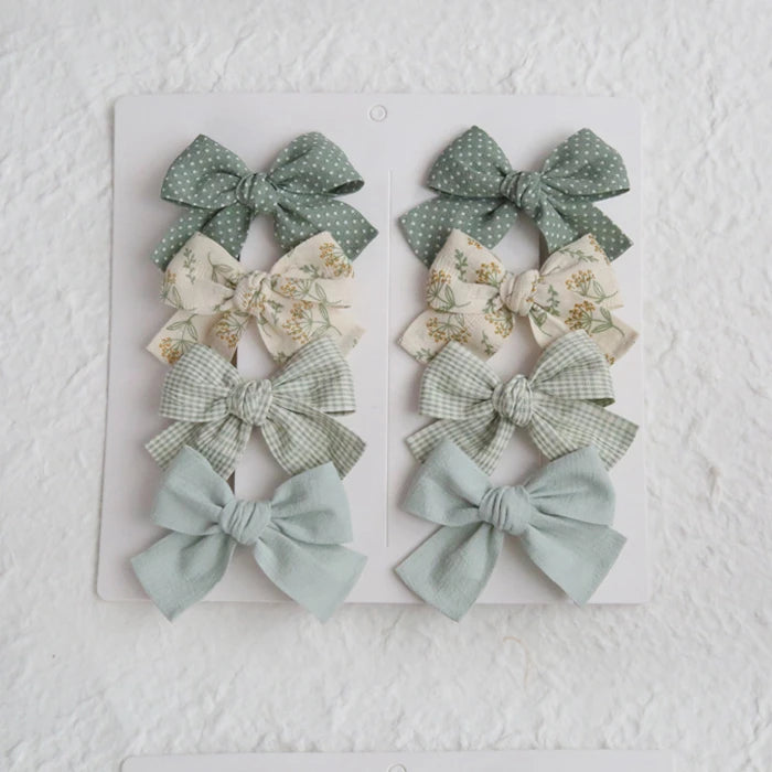 Set of 8 girls' hair clips with elegant cotton bows in sage green, polka dot, floral, and gingham patterns.