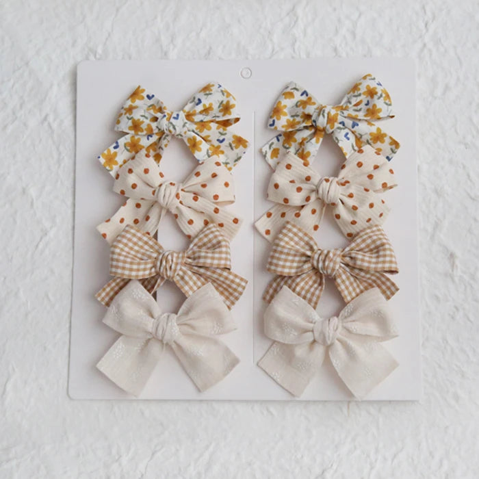 Set of 8 girls' cotton hair bows in floral, polka dot, gingham, and solid beige designs.