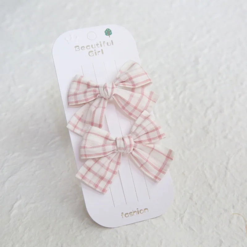 Two pink and white plaid cotton bow hair clips for girls on a white card.