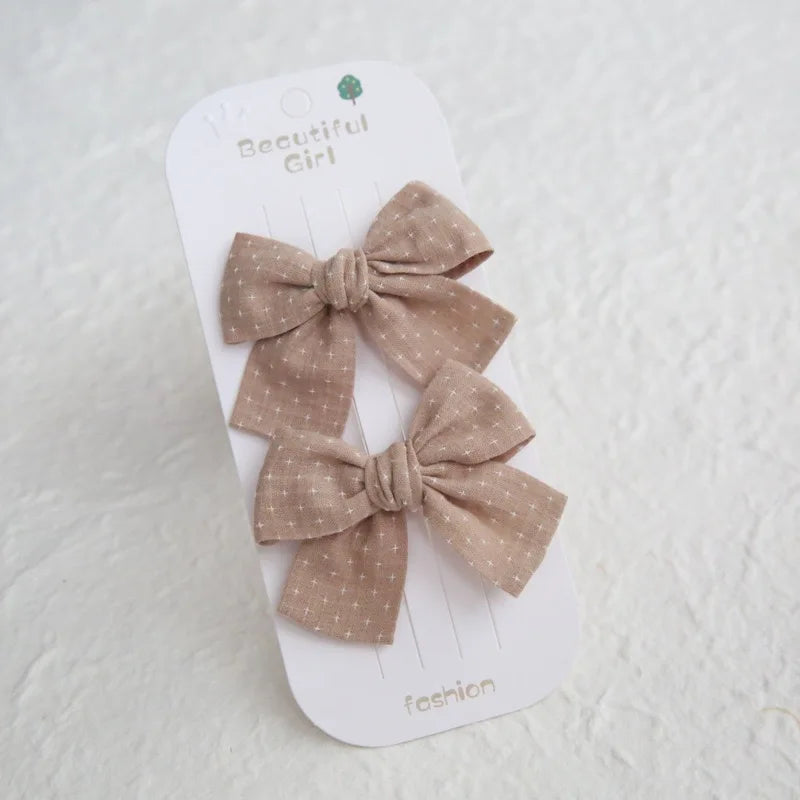 Two beige cotton hair bows with white cross patterns on a "Beautiful Girl" card.