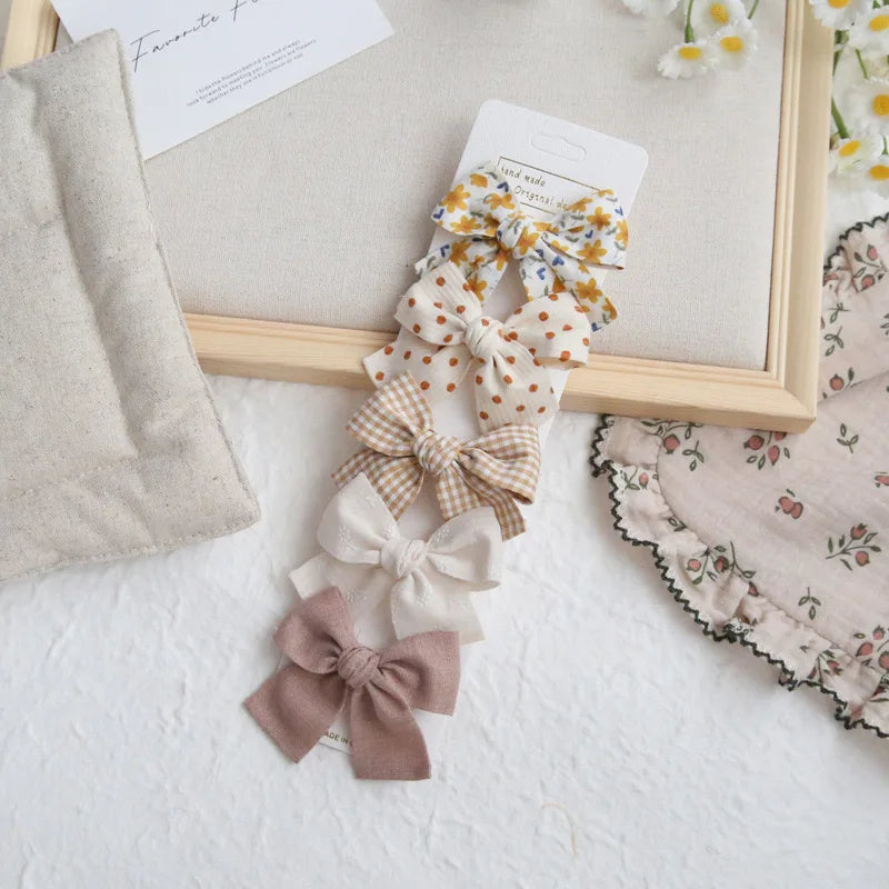 Set of five cotton hair bows for girls in various patterns: floral, polka dot, gingham, solid cream, and solid brown.