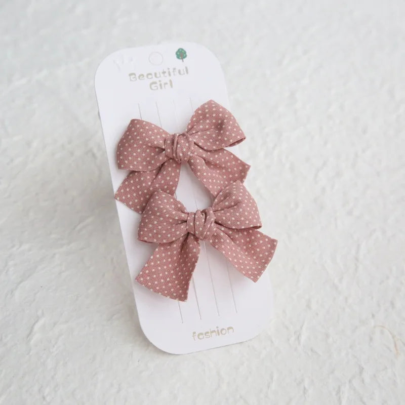 Two pink cotton hair bows with white polka dots on a white card.