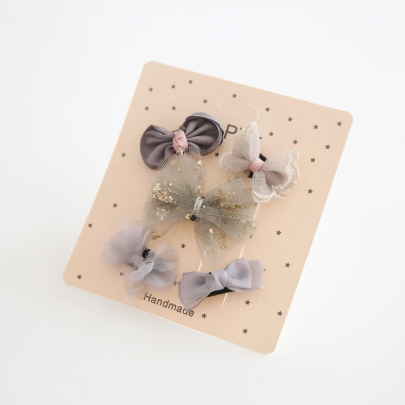 Set of five gray and pink baby hair clips with decorative bows, some with glitter.
