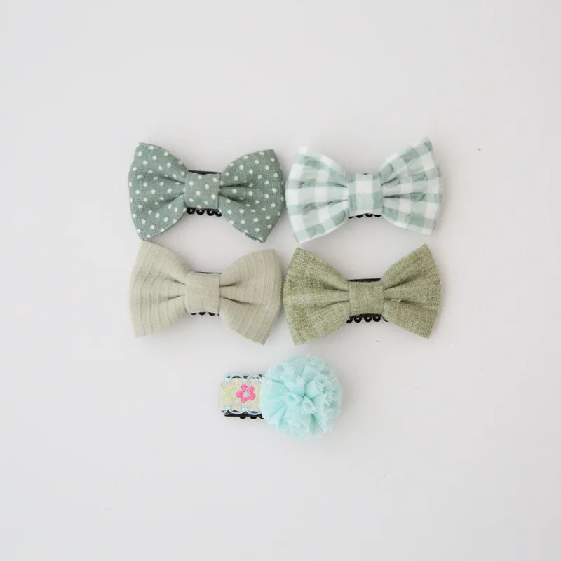 Set of five baby hair clips: two green bow clips (polka dot, gingham), two solid green bow clips, and one light blue pom-pom clip.