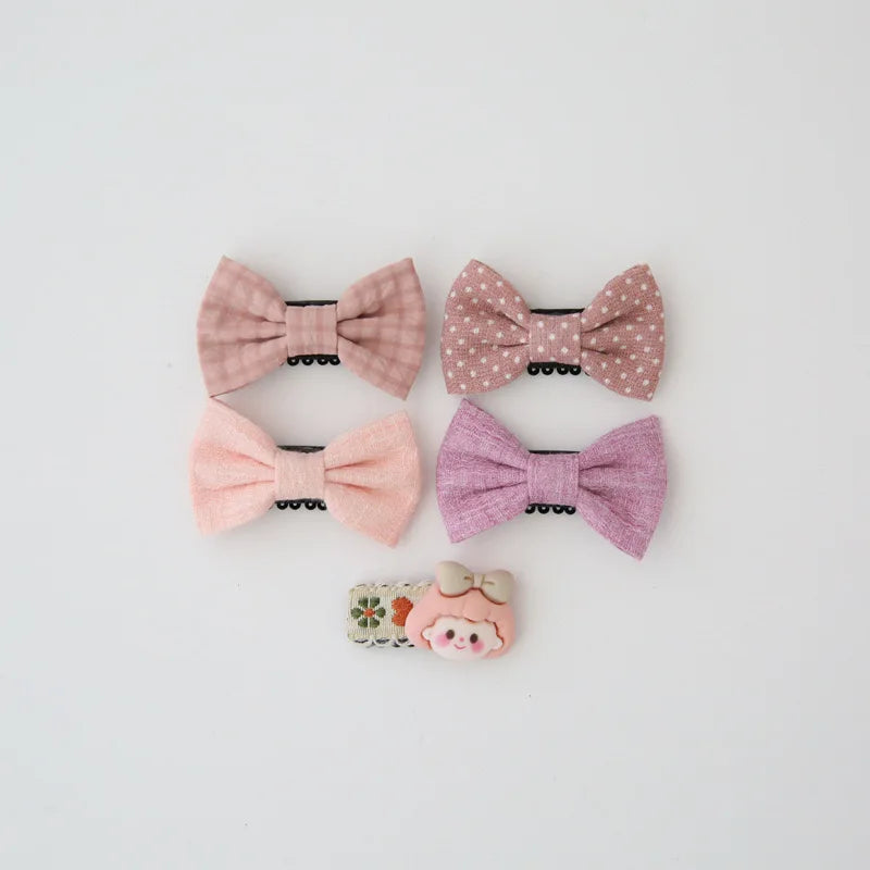 Set of four pastel pink and purple bow hair clips for babies, plus one clip with a cute girl character.