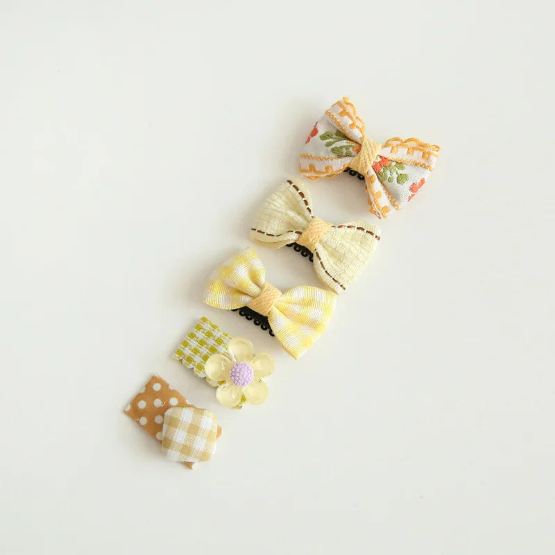 Assortment of five baby hair clips with decorative bows in yellow, white, and orange floral and plaid patterns.