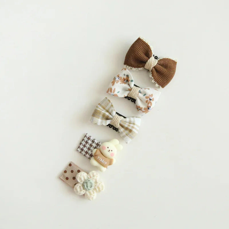 Set of five adorable baby hair clips: brown corduroy bow, floral bow, plaid bow, bear clip, and flower clip.