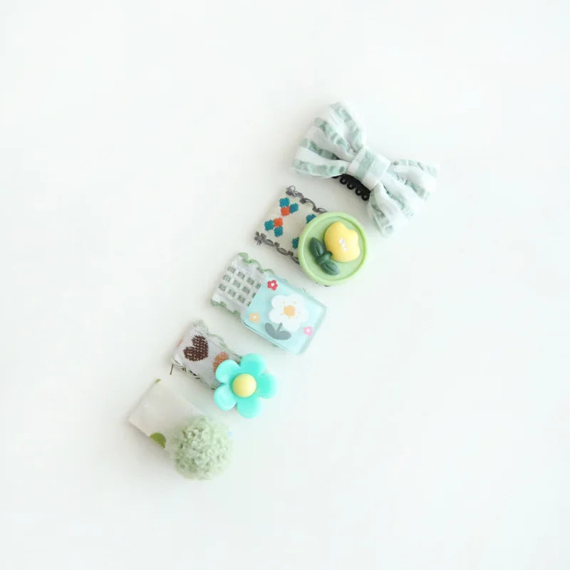 Set of five pastel baby hair clips: striped bow, yellow egg, blue flower, heart, and green pom-pom.