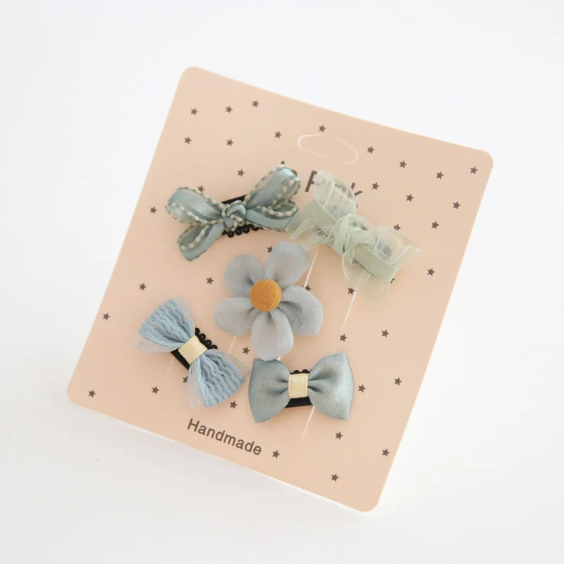 Set of five pastel blue and green baby hair clips with bows and a flower design on a pink card.