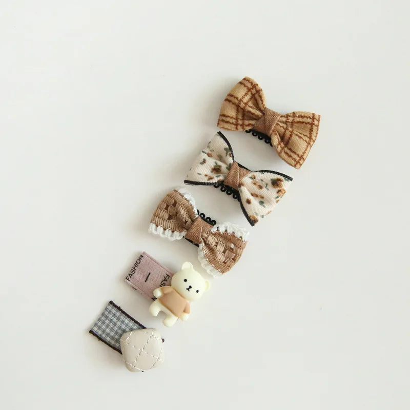 Set of four cute baby hair clips: three bow clips in plaid, floral, and knit patterns, plus a teddy bear clip.