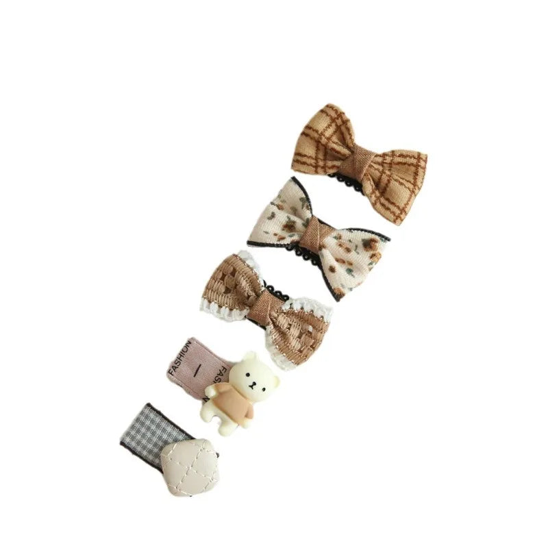 Set of five cute baby hair clips: three brown bow clips with patterns and lace, one pink clip with "FASHION," and one white teddy bear clip.