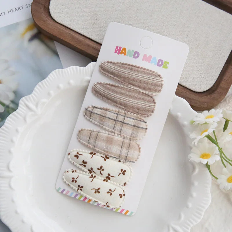 Set of 6 handmade cotton hair clips for babies and girls, featuring plaid, striped, and floral patterns in neutral tones.
