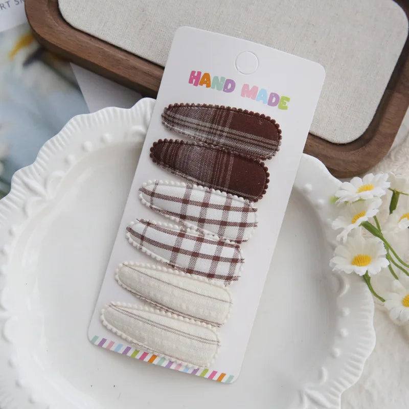 Handmade set of 6 fabric hair clips for babies and girls, featuring brown plaid, white plaid, and cream striped designs.