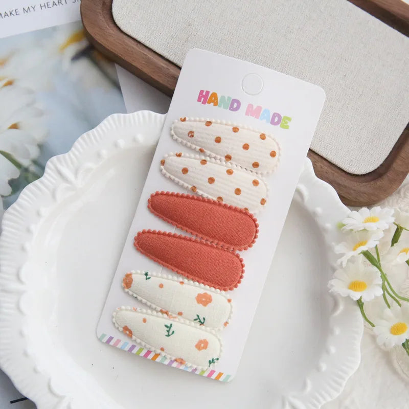 Set of 6 handmade fabric hair clips for babies and girls, featuring polka dots, solid coral, and floral patterns.