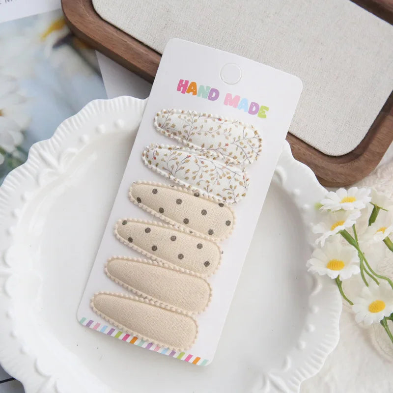 Handmade set of 6 fabric hair clips for babies and girls, featuring floral, polka dot, and solid beige designs.