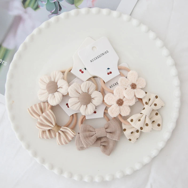 Handmade cotton hair ties for girls, featuring beige floral and bow designs on a white plate.