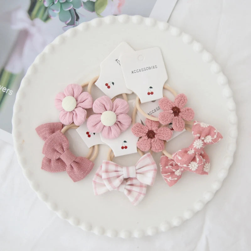 Handmade pink cotton hair ties for girls, featuring floral and bow designs on a white plate.