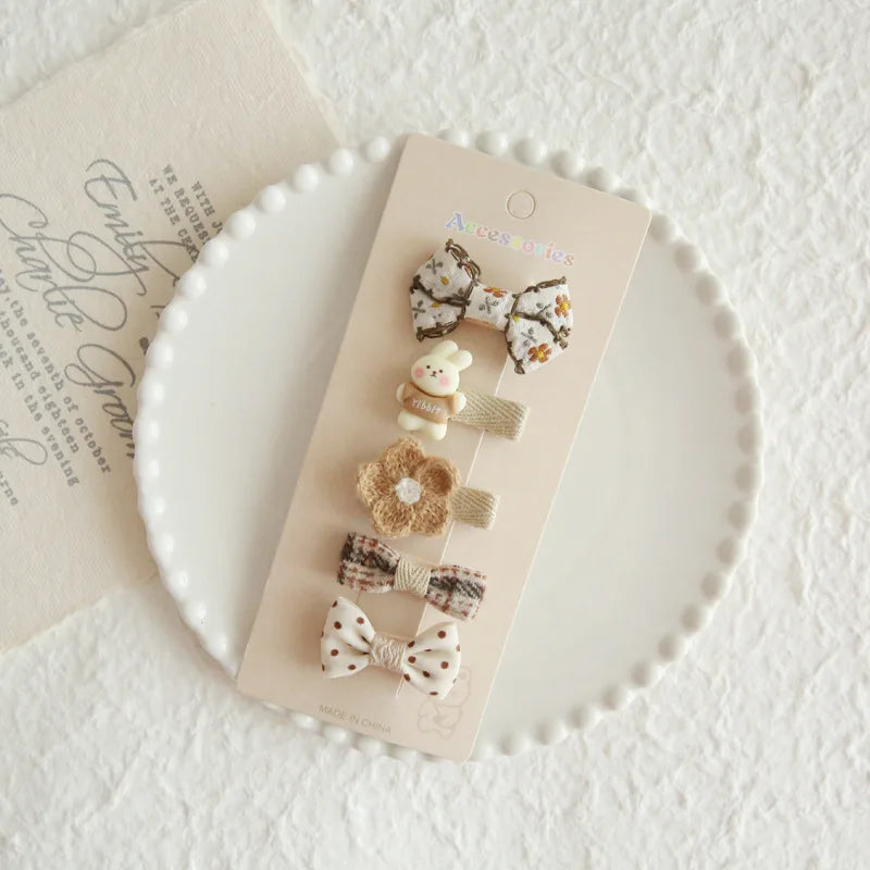 Set of 5 baby girl hair clips: floral bow, rabbit, crochet flower, plaid bow, and polka dot bow.