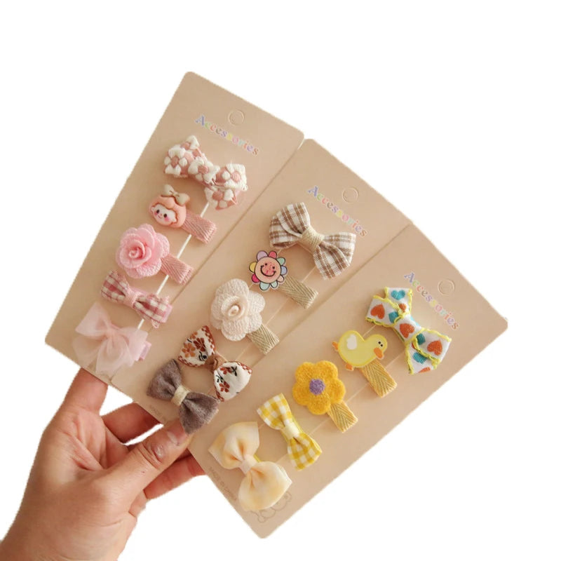 Hand holding three sets of 5 colorful floral and bow hair clips for babies and girls.