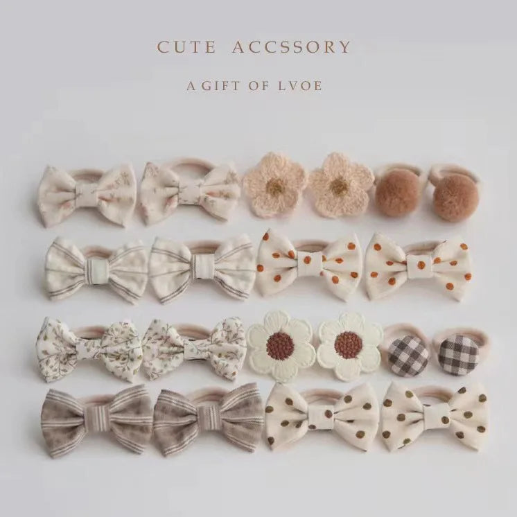 Set of 10 girls' hair ties and clips in various beige, brown, and cream designs, including bows, flowers, and pompoms.