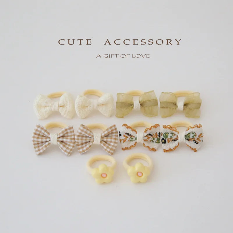 Set of 10 girls' hair ties and clips: cream bows, green sheer bows, plaid bows, floral bows, and yellow flower rings.