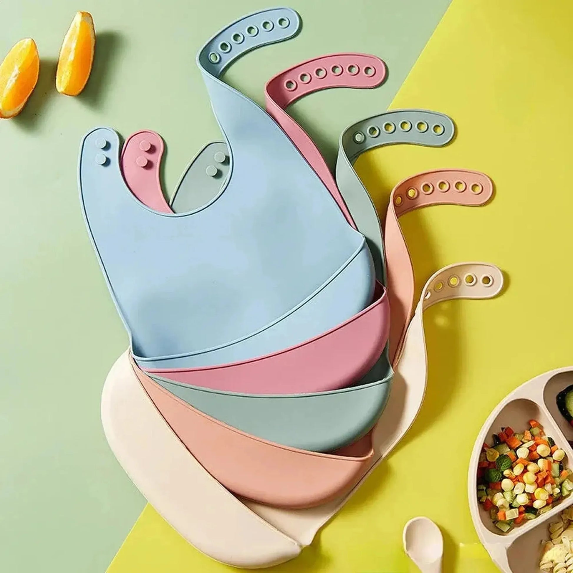 Stack of colorful silicone baby bibs in blue, pink, green, and cream, with adjustable neck closures.