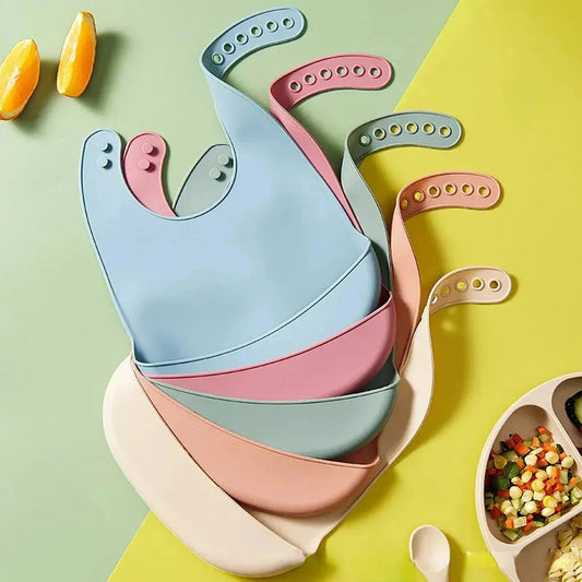 Stack of colorful silicone baby bibs in blue, pink, green, and cream, with adjustable neck closures.