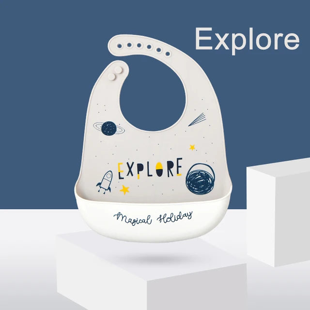 Adjustable gray silicone baby bib with "Explore" space theme and food-catching pocket.