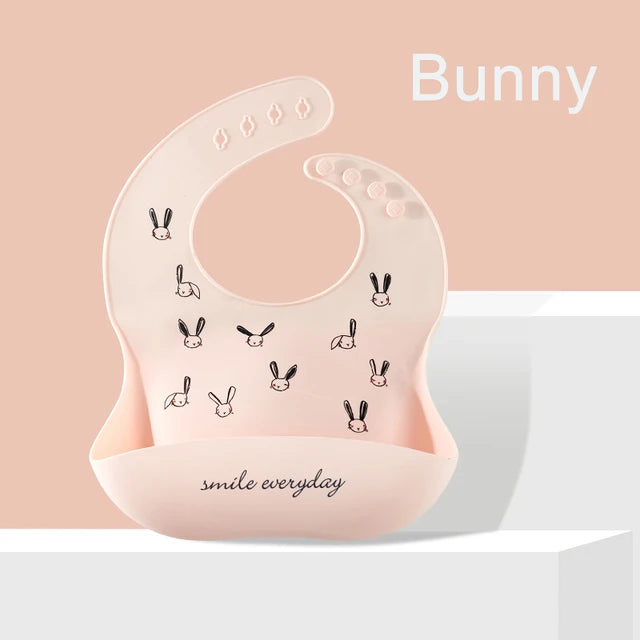Pink silicone baby bib with bunny print, adjustable neck, and deep food-catching pocket.