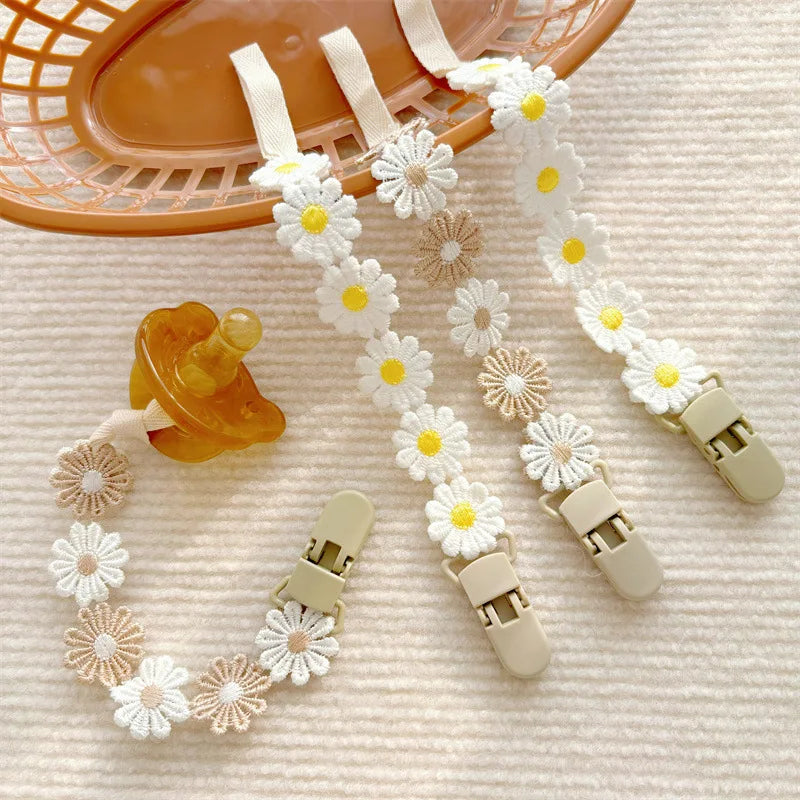 Daisy flower pacifier clips in white and beige polyester, with a brown pacifier.