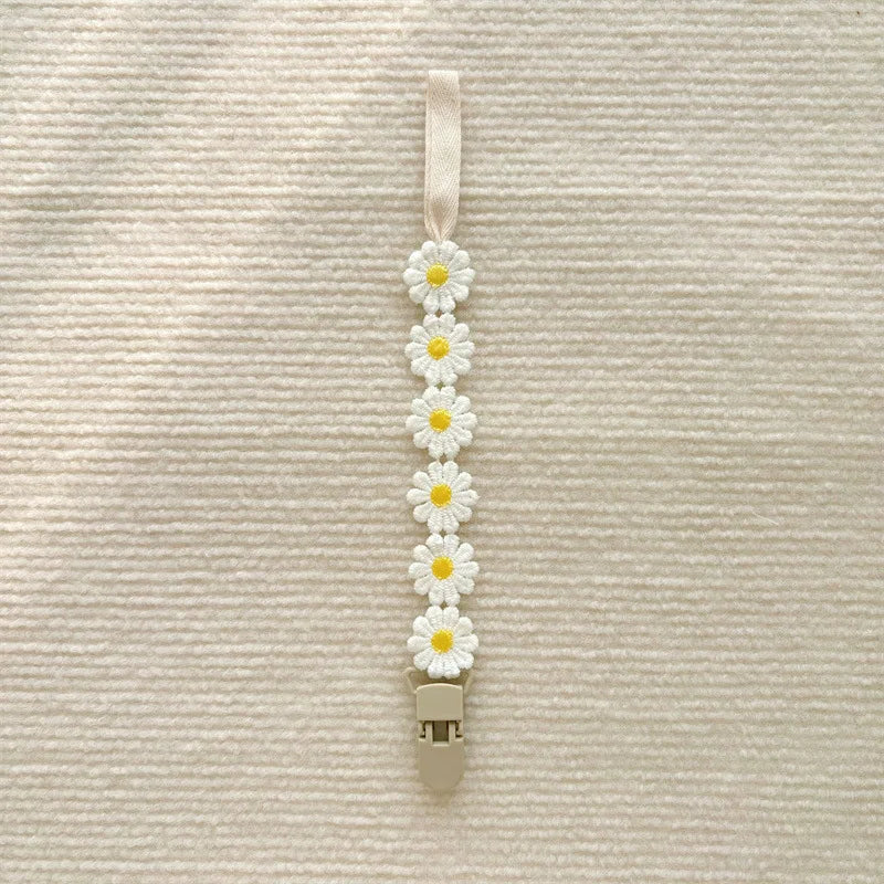 Beige pacifier clip with a row of white and yellow daisy flowers, 25cm long.