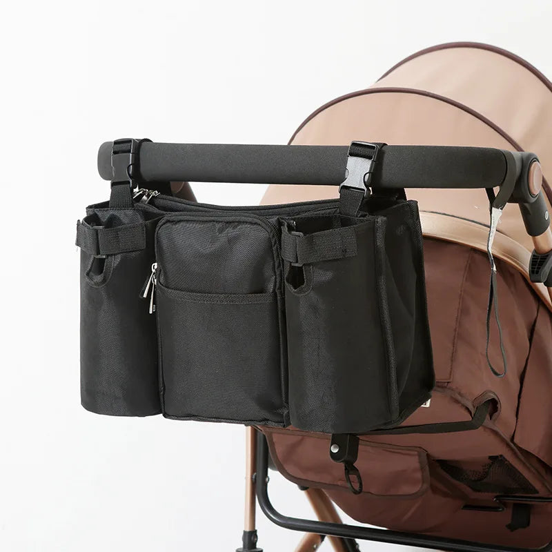 Black waterproof stroller organizer bag with multiple compartments and bottle holders, attached to a brown stroller.