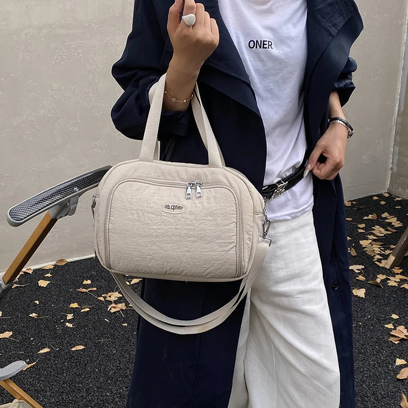 Stylish beige polyester diaper bag with silver zippers and adjustable strap, held by a person.