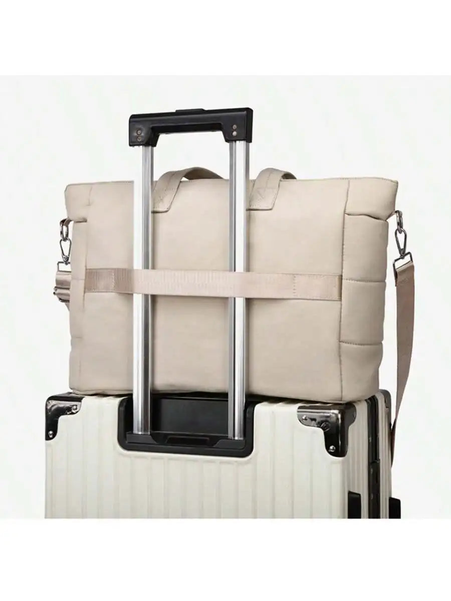 Stylish beige diaper tote bag with shoulder strap, resting on a light-colored suitcase handle.