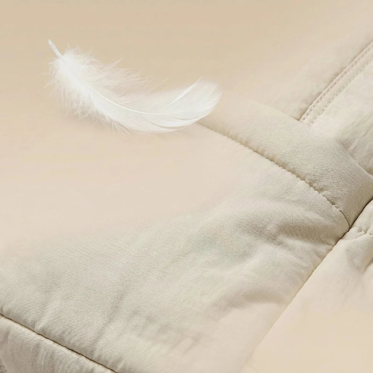 Light beige synthetic leather diaper bag with a soft, quilted texture and a white feather.