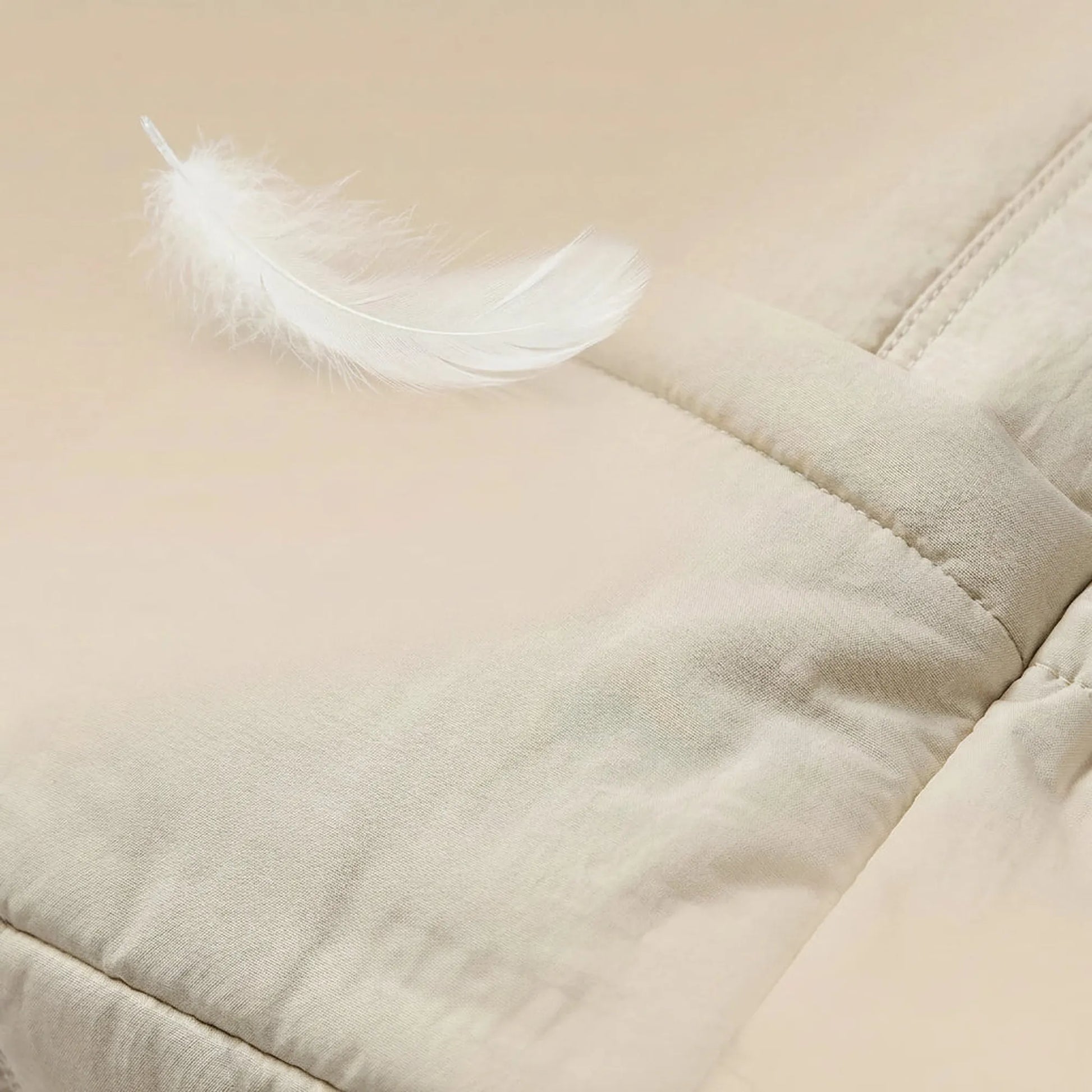 Light beige synthetic leather diaper bag with a soft, quilted texture and a white feather.