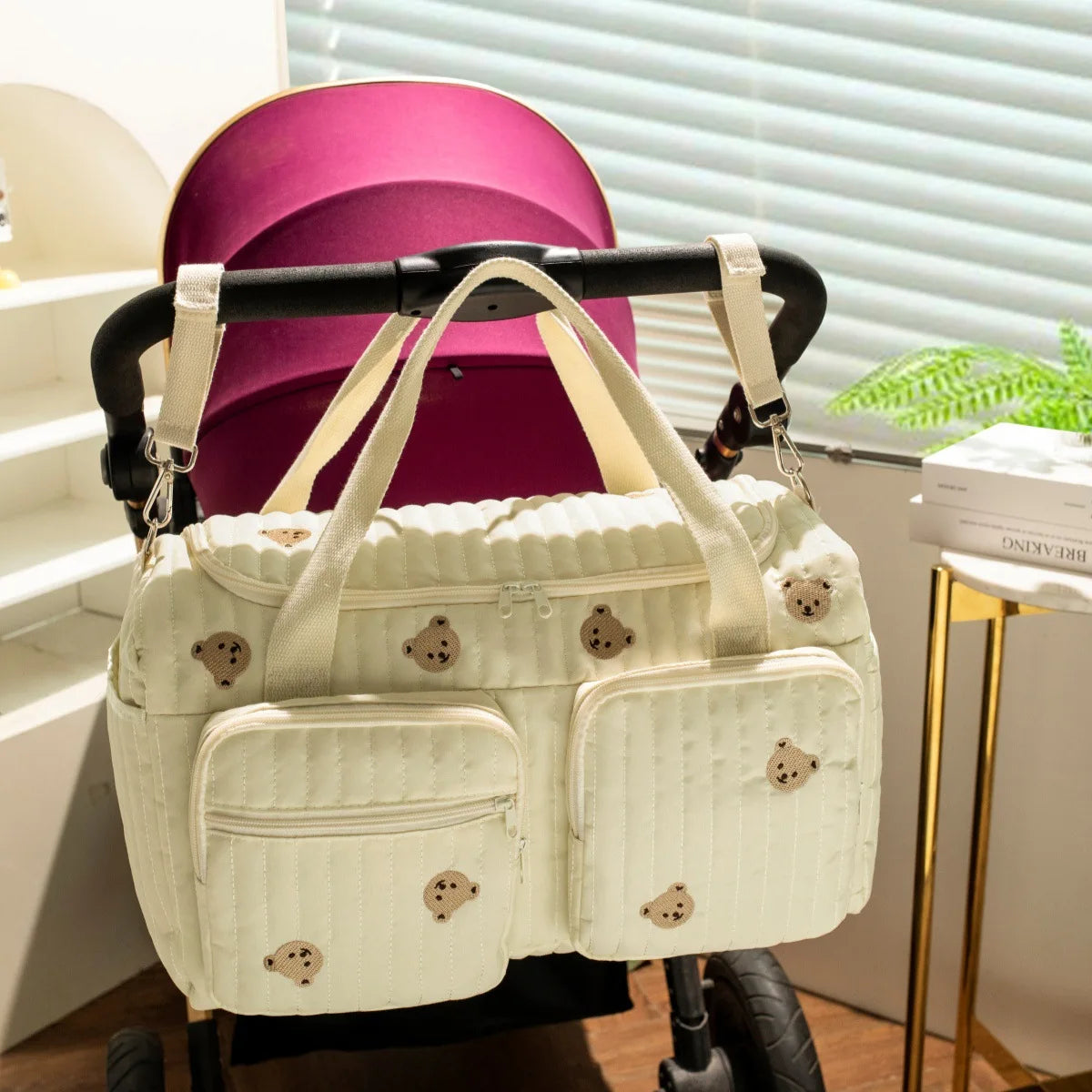 Quilted light green cotton diaper bag with embroidered teddy bears, zipper closure, hanging on a stroller.