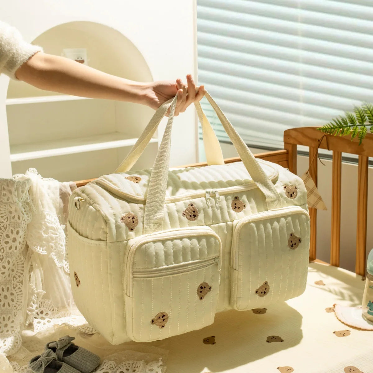 Quilted cream cotton diaper bag with embroidered teddy bears, zipper closure, and front pockets.