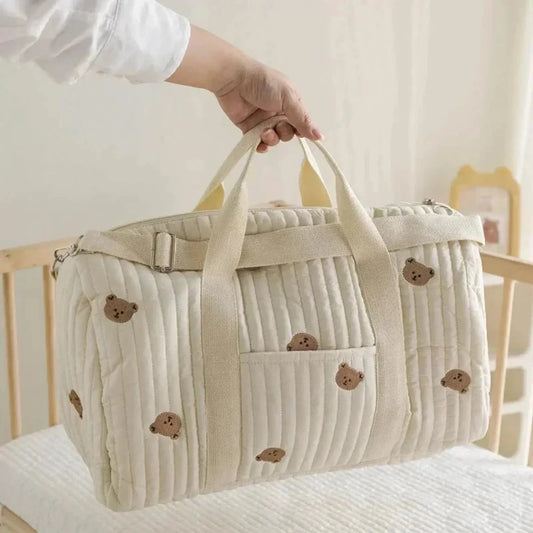 Cream quilted cotton diaper bag with embroidered teddy bears, front pocket, and shoulder strap.