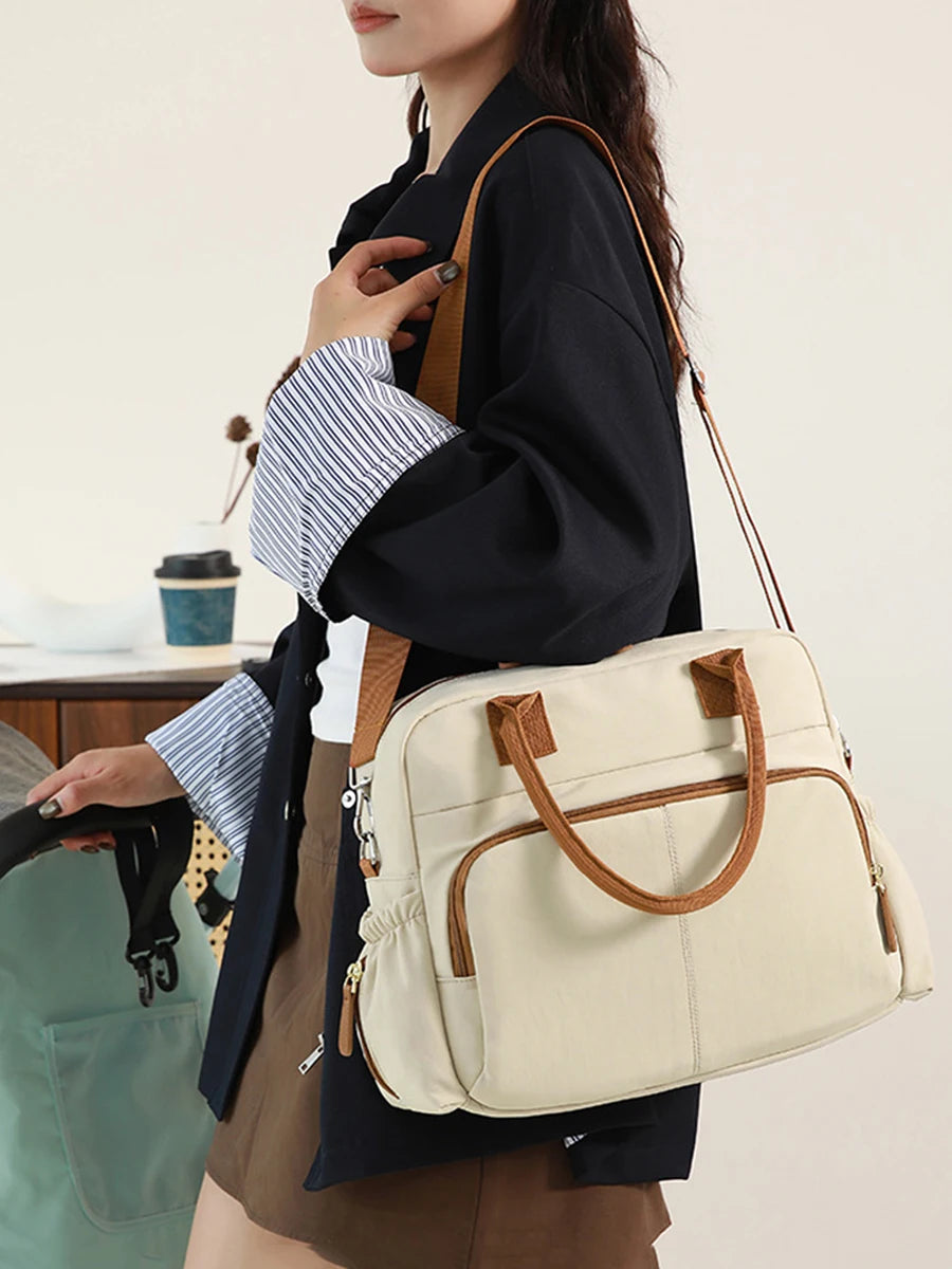 Stylish beige diaper bag with brown trim, carried by a woman pushing a stroller.