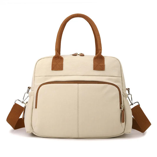 Beige diaper bag with brown handles and shoulder strap, featuring front pockets and a modern design.