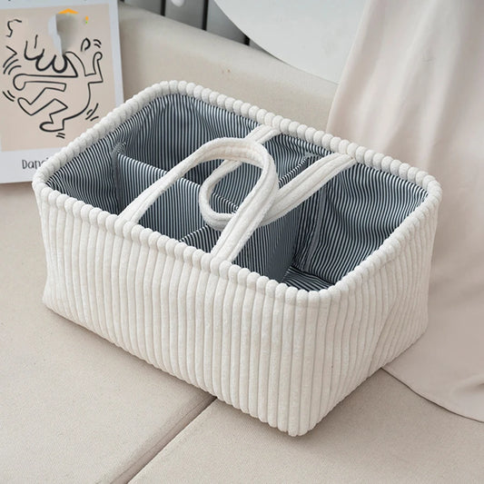White corduroy diaper caddy with striped interior, multiple compartments, and a central handle.