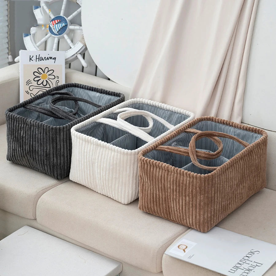 Three corduroy diaper caddies in gray, white, and brown with striped interiors and handles.