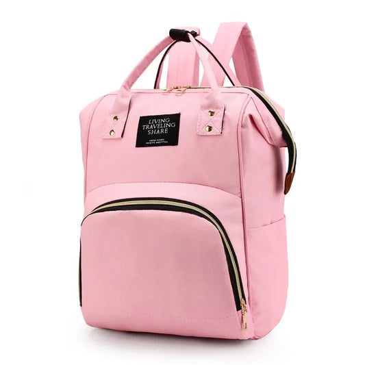 Pink canvas diaper backpack with top handles, front zipper pocket, and side pockets.